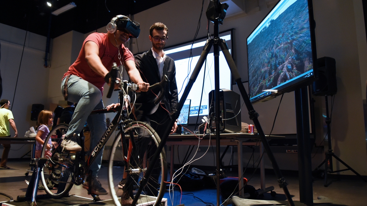 Kyle Hoefer presents his virtual reality biking system to another student at the digital culture showcase