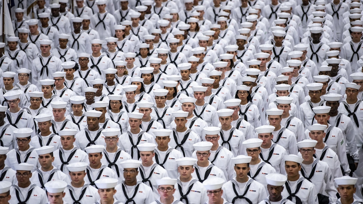 Several neat rows of people dressed in white U.S. Navy regalia.