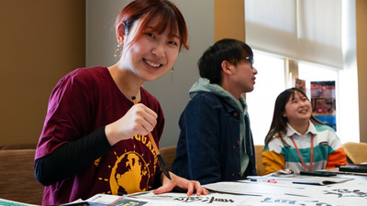 Student smiling at camera while holding a calligraphy brush.