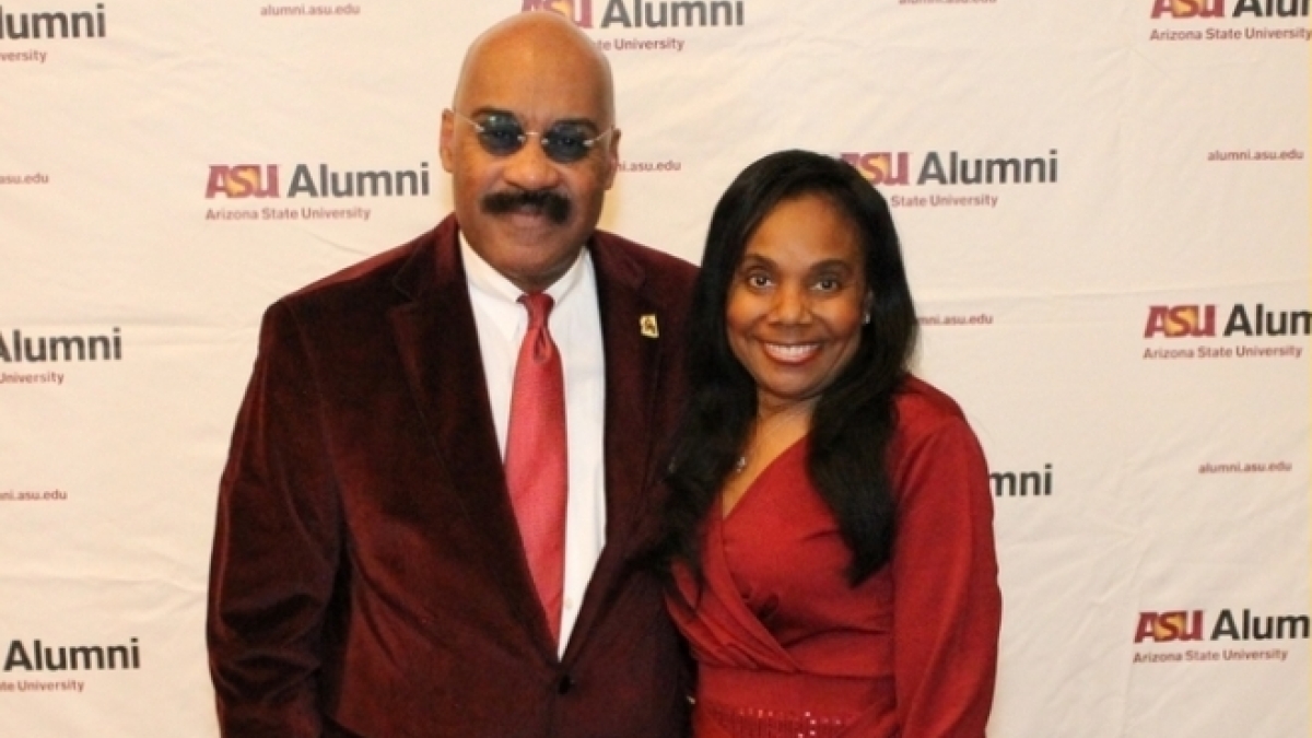 ASU alum Vada Manager poses with a woman in front of a wall with the words "ASU Alumni."