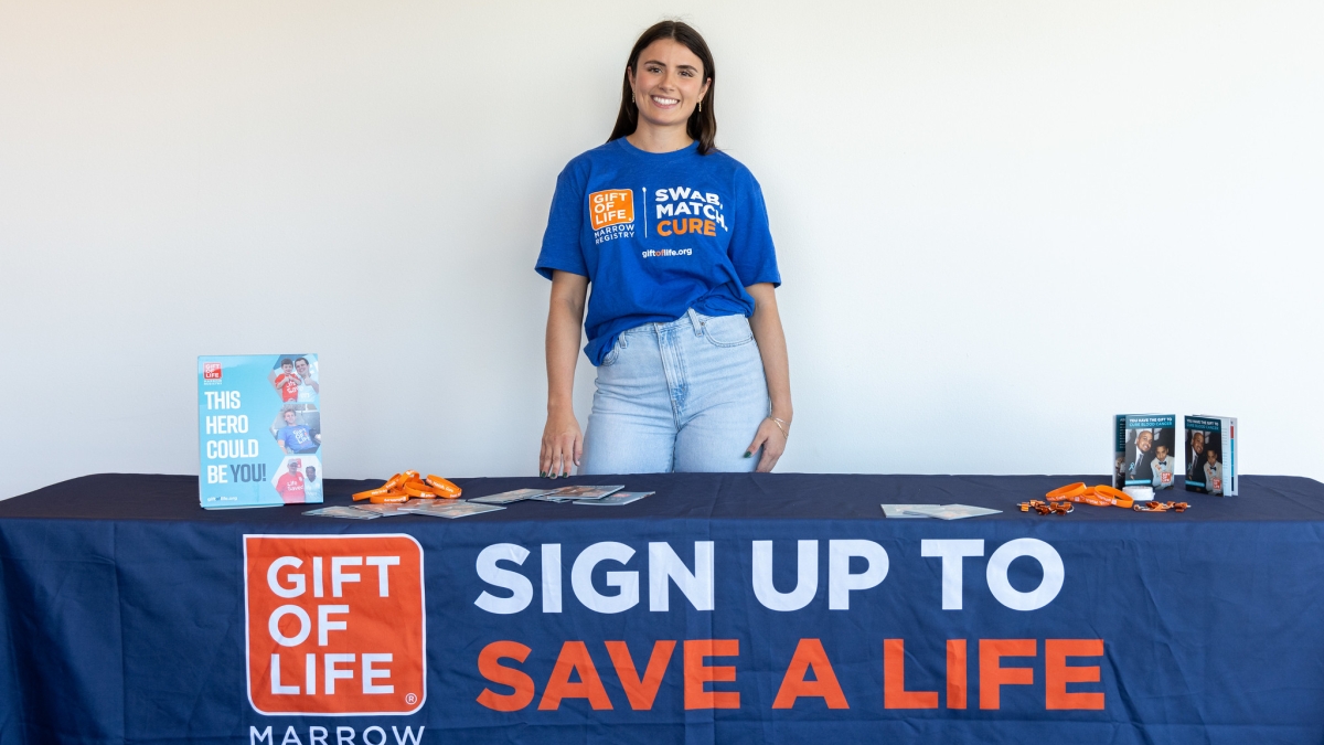 A woman with dark hair stands behind a table with a Gift of Life Registry table cloth.
