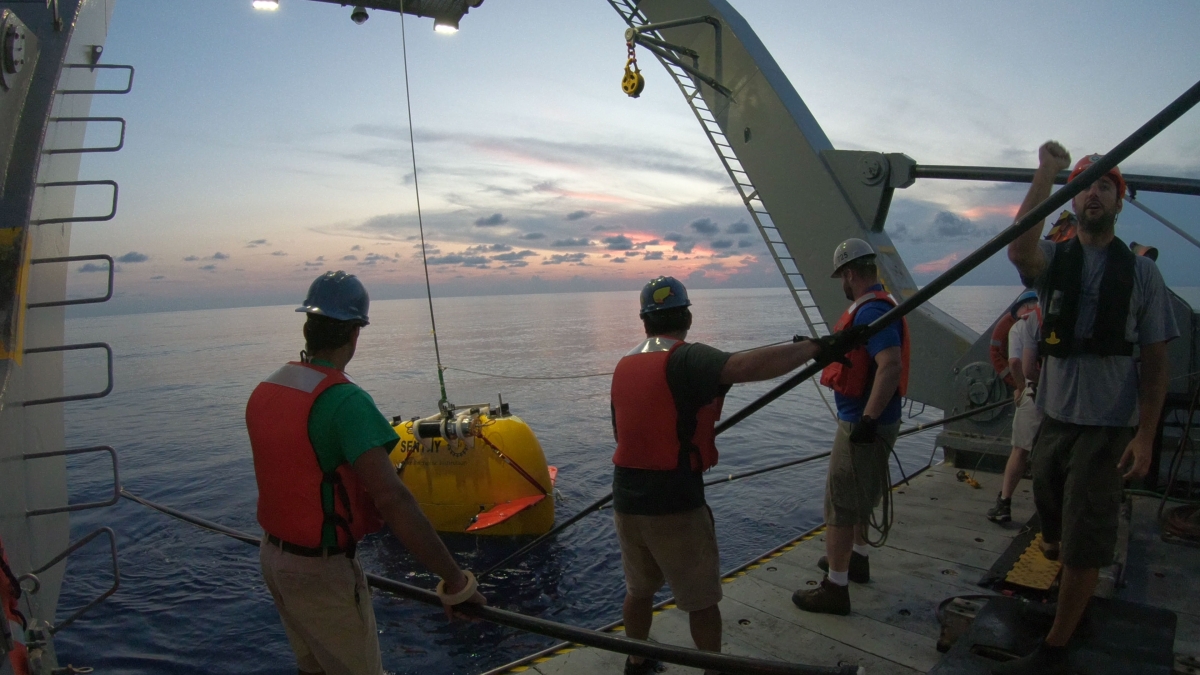 Crew on a ship retrieve a smaller, autonomous underwater vehicle out of the ocean using a winch
