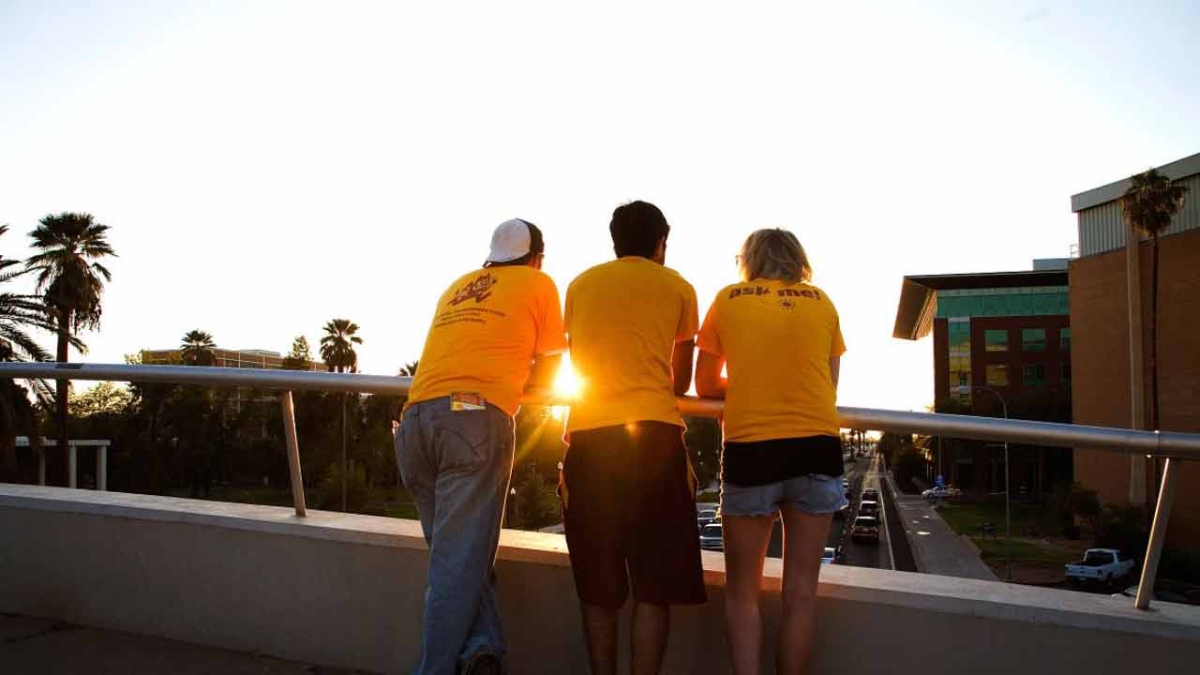 3 ASU students on a bridge look over University Drive as the sun sets
