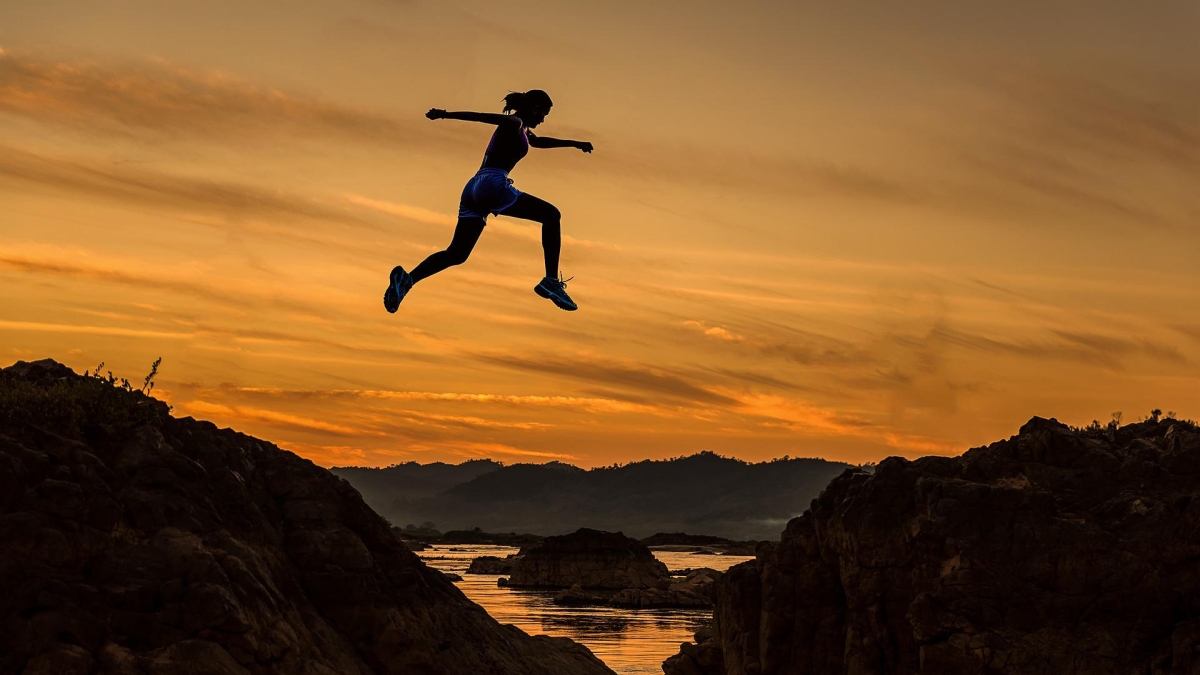 Silhouette of a person jumping across an expanse in a rocky terrain.