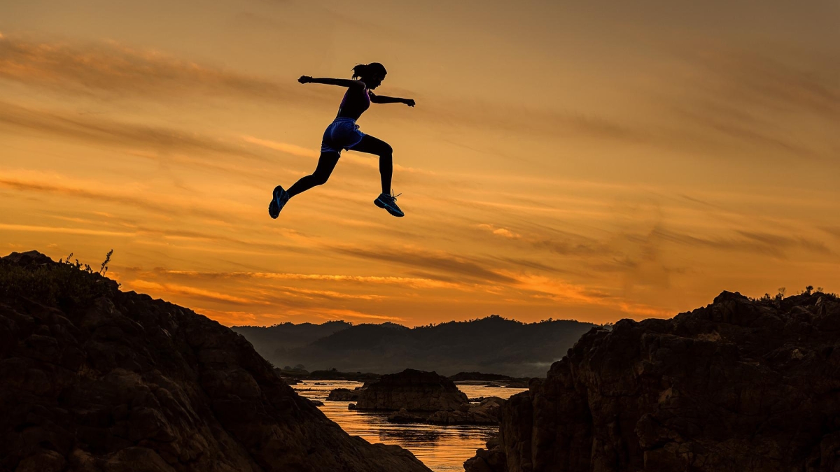 Silhouette of a person jumping across an expanse in a rocky terrain.
