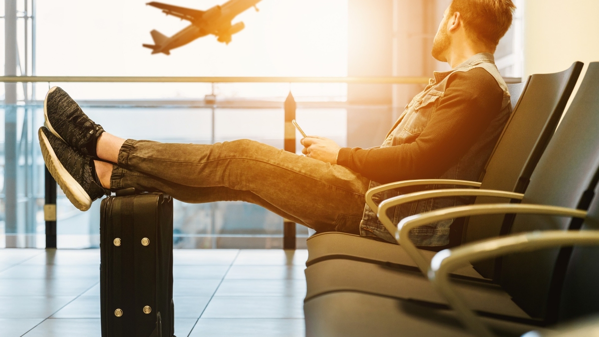 Man sitting in airport with luggage looking at plane take off