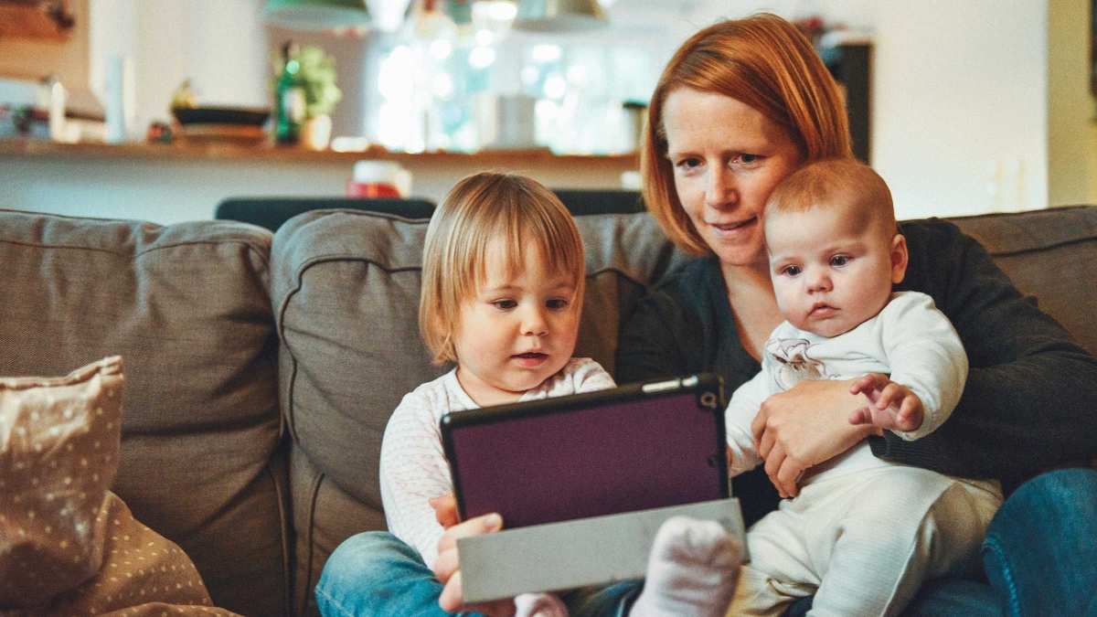 A mother sits on the couch with her two young children looking at a tablet