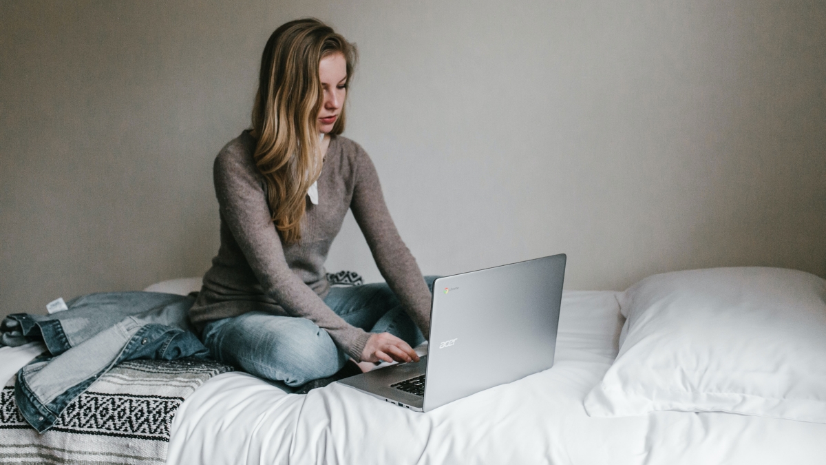A woman works on a laptop while sitting on a bed