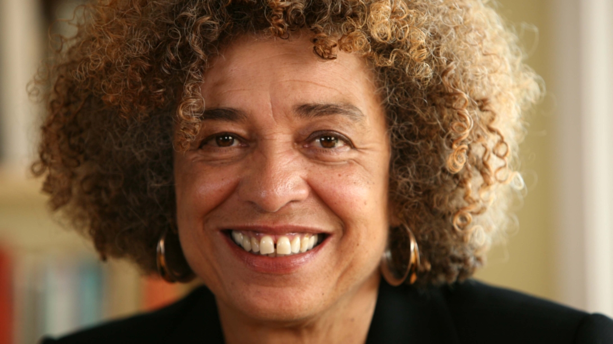 Headshot of Angela Davis smiling in a black blazer in front of a blurred bookcase background.