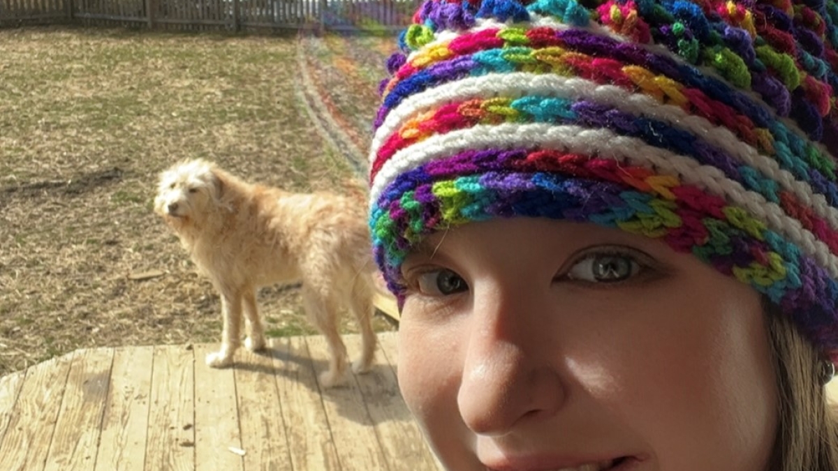 Anna Gutmann is photographer wearing a mutli-colored knitted hat next to her big golden-colored dog.