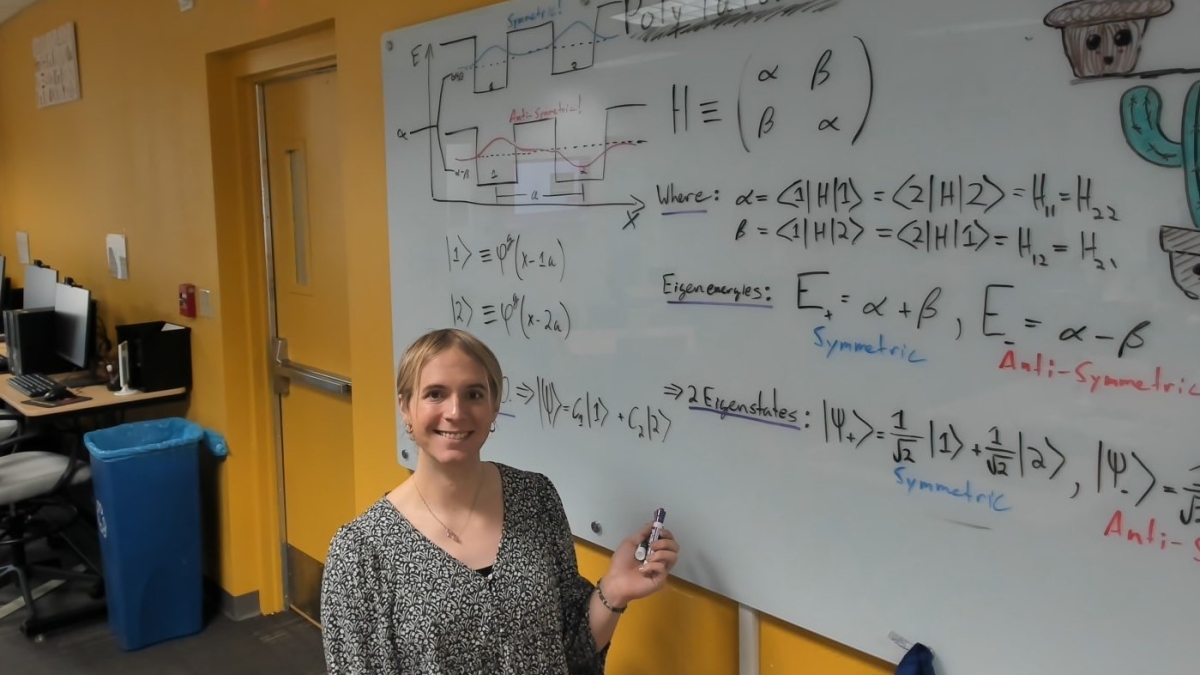 ASU College of Integrative Sciences and Arts applied physics graduate Addison Olsen smiles while standing in front of whiteboard.