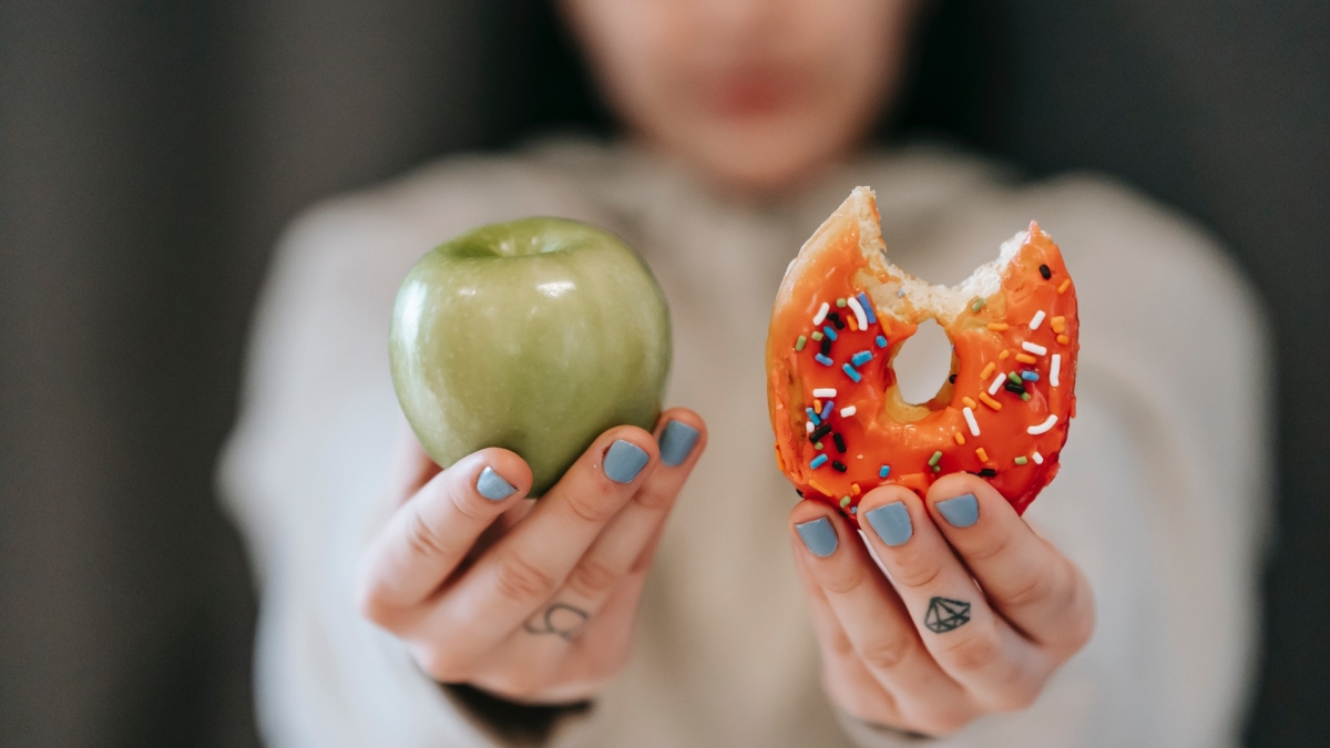 Woman holding out an apple and a donut.