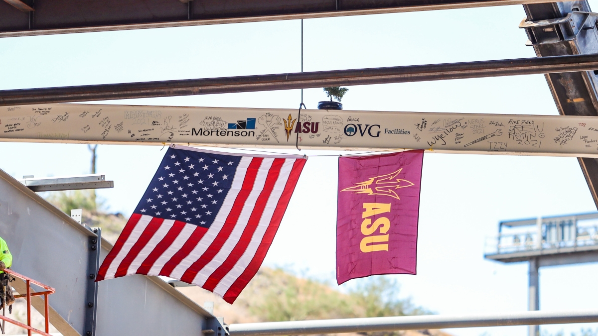 A steel beam covered in signatures and attached to two flags is being lifted by a crane