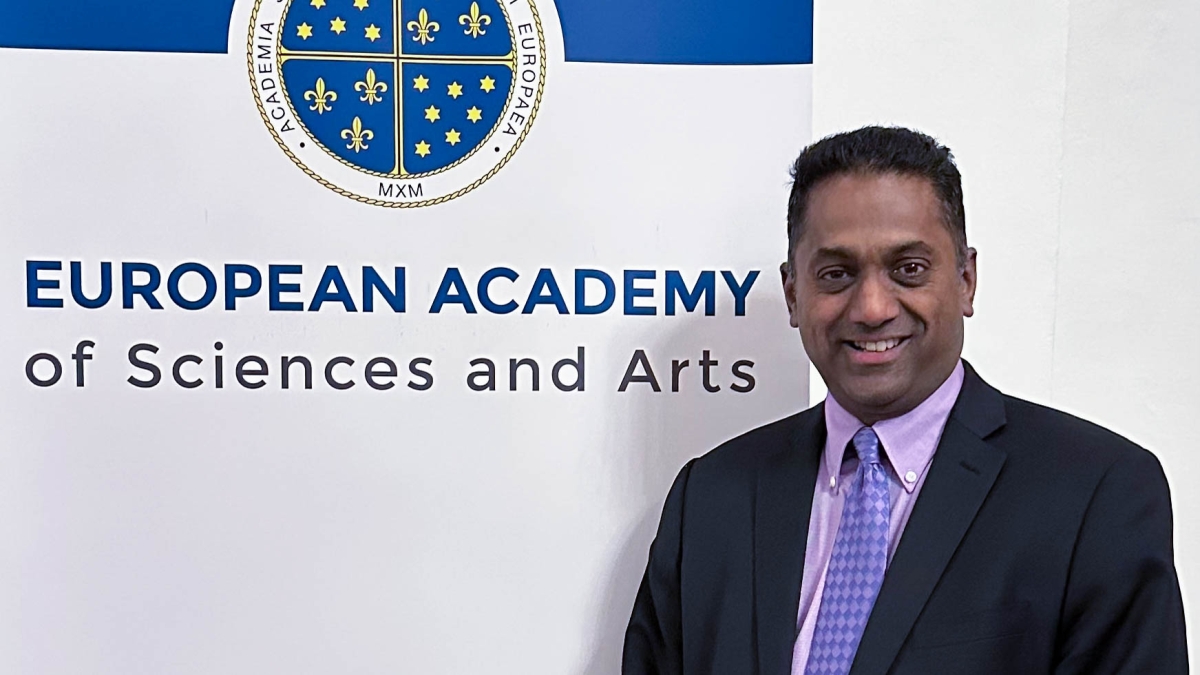 ASU Professor Samuel Ariaratnam at smiles next to a sign reading "European Academy of Sciences and Arts."