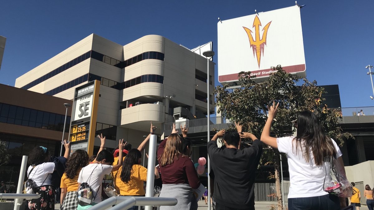 Foster youth with their backs turned giving Forks Up in front of Sun Devil Stadium