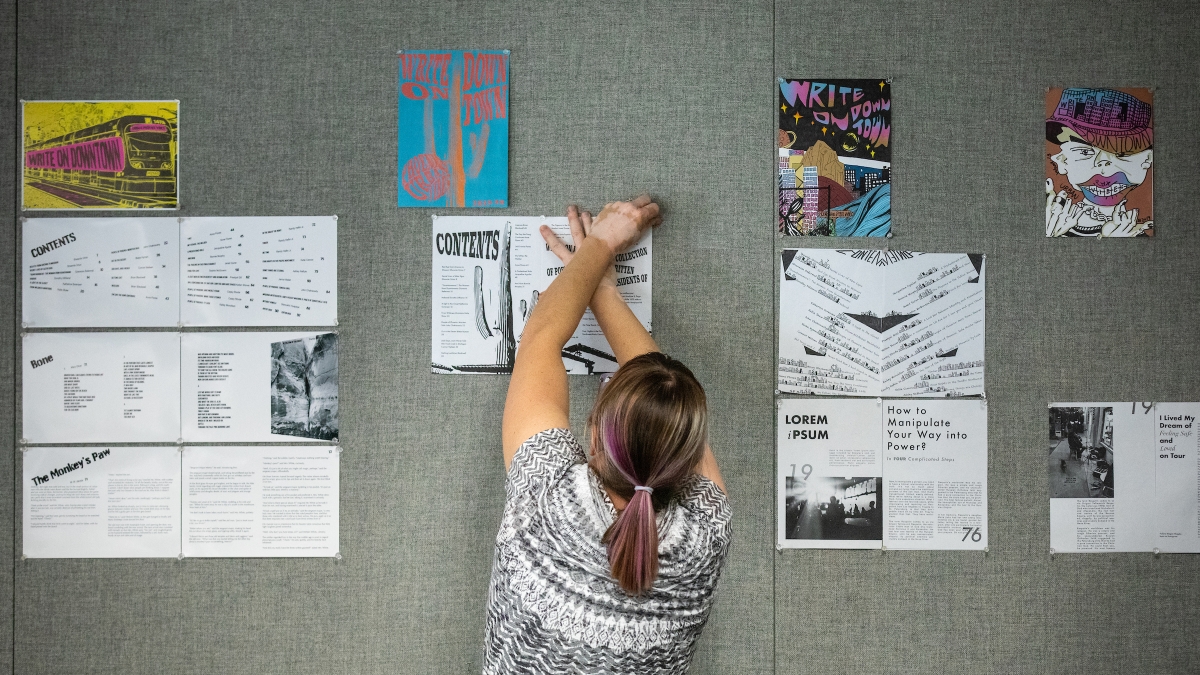shot of a woman from the back, pinning an illustration to a wall with many illustrations already pinned on it