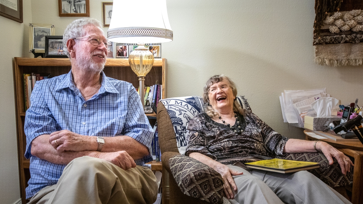 an elderly man and woman sitting in a living room laughing