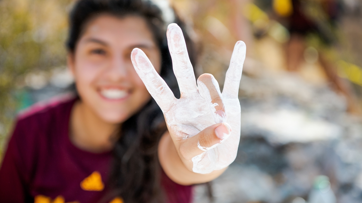 student holding up a pitchfork gesture with her hand covered in white paint