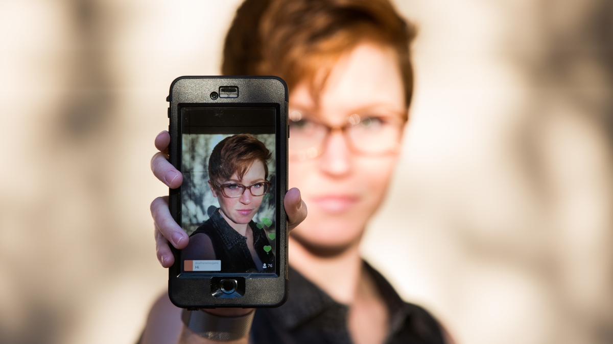 A woman holds up a phone that has her photo on it.