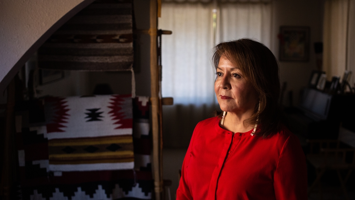 woman in a red shirt looking off camera to the left with a Navajo blanket in the background