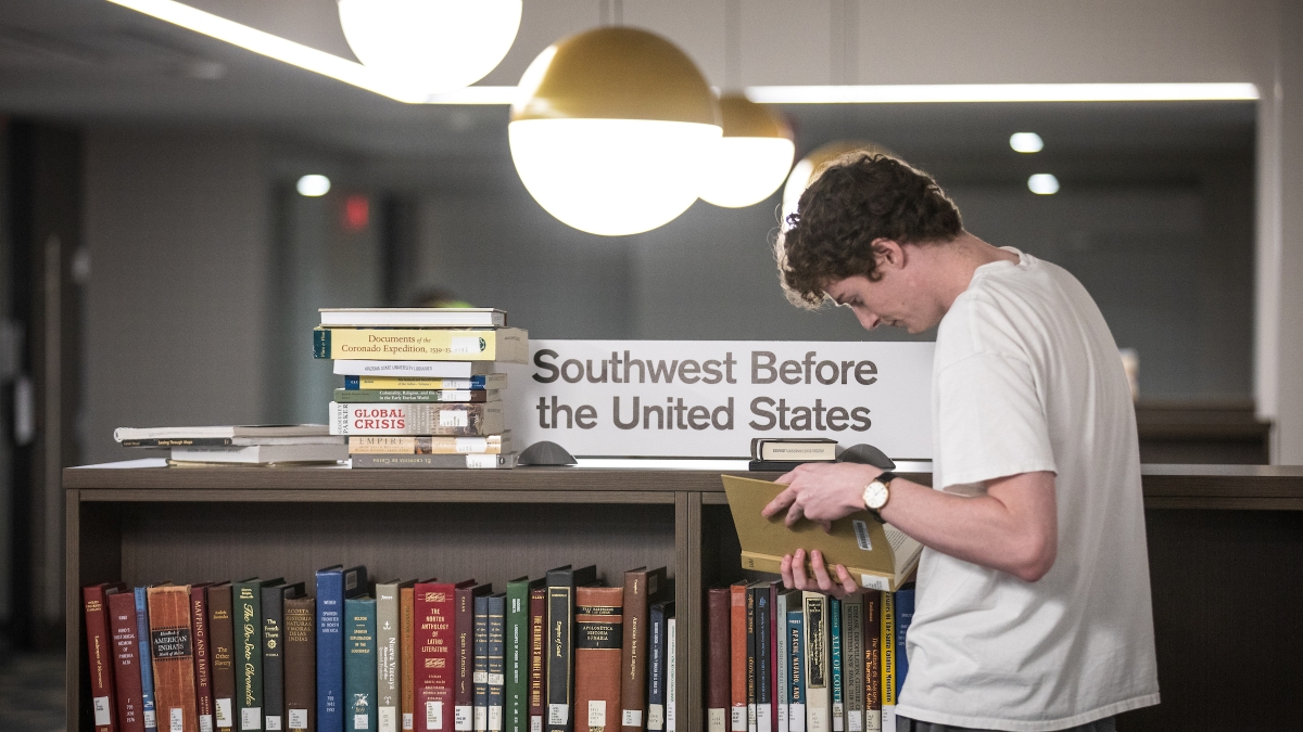 student stacking books on shelf in library