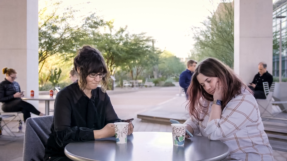two women sit next to each other at a table while looking at their smartphones