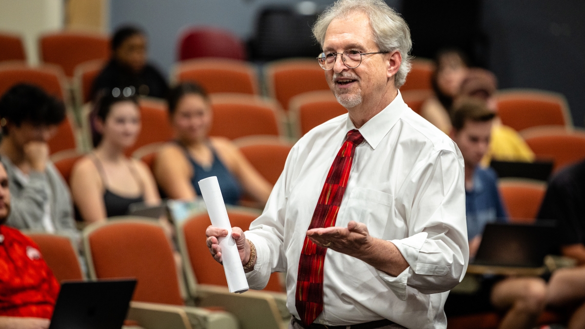 Professor in a white shirt and red tie speaking to students in a classroom.