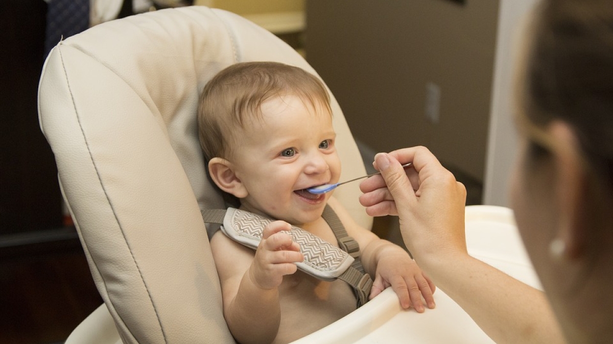 baby in high chair being fed by mom with a spoon