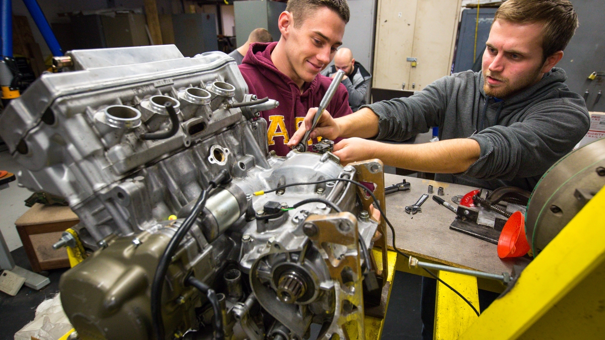 Two students work on a car engine.