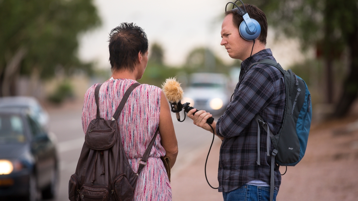 man recording a woman speaking next to a freeway