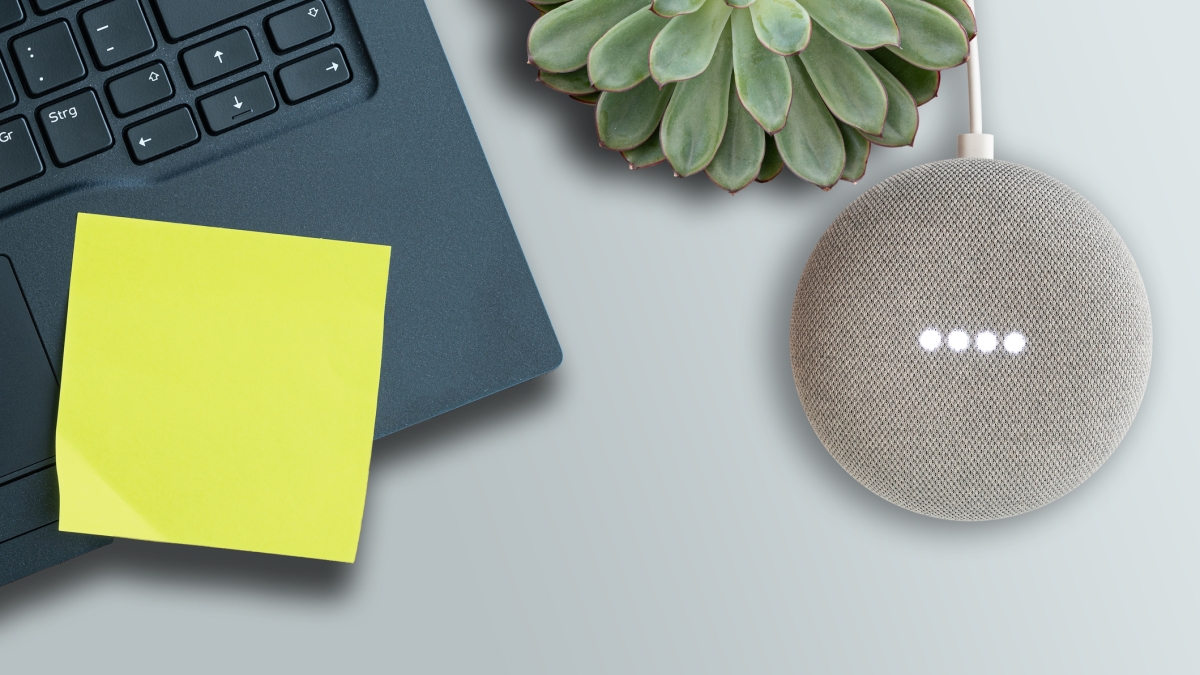 An overhead shot of a laptop with a post it note, a plant and a Google speaker