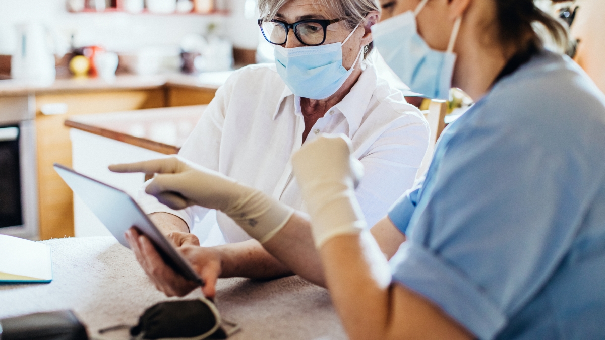 two health care workers wearing masks while looking at a tablet
