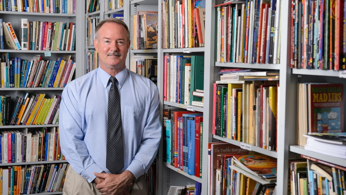 ASU English Professor James Blasingame standing in his office surrounded by shelves of books