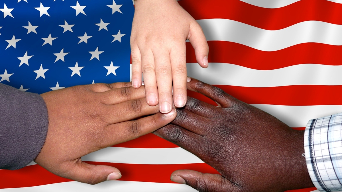 hands of varying skin tones in front of the American flag