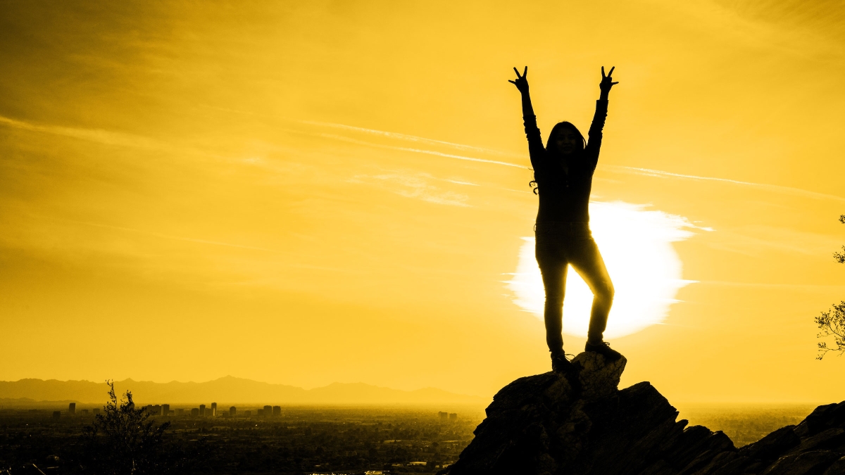woman on mountain with sun behind her making pitchforks with hands