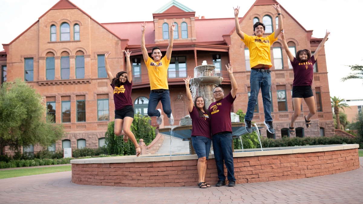 A family of five in maroon and gold celebrates in front of the Old Main fountain