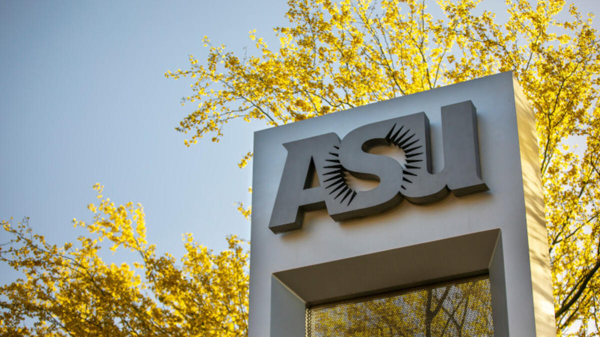 Sign with the letters "ASU" on a campus, surrounded by a tree in bloom.