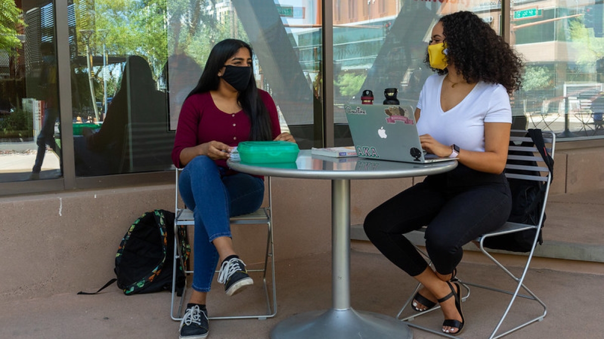 Two women at a table outside wearing masks on ASU's campus