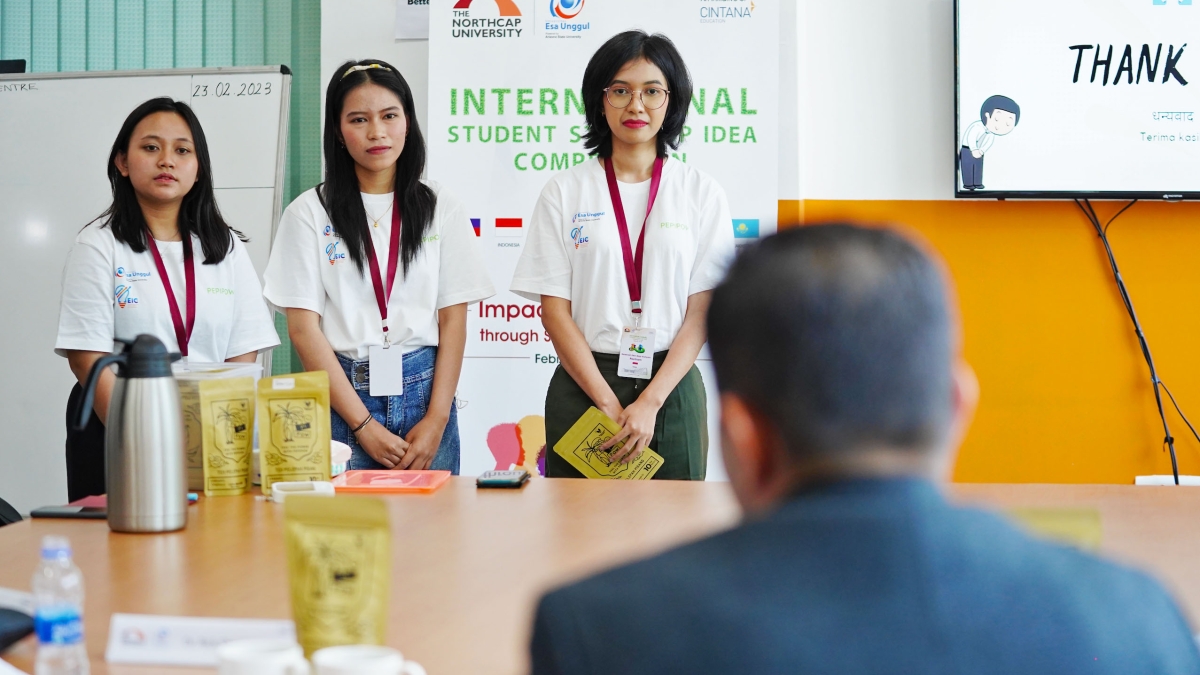 Three students standing in front of a competition judge sitting at a table.