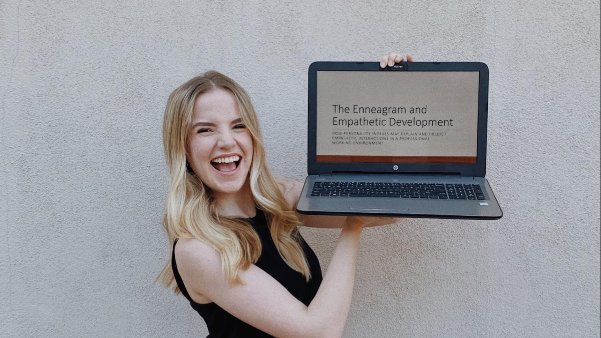 Claire holding up a laptop on a screen related to her field of study