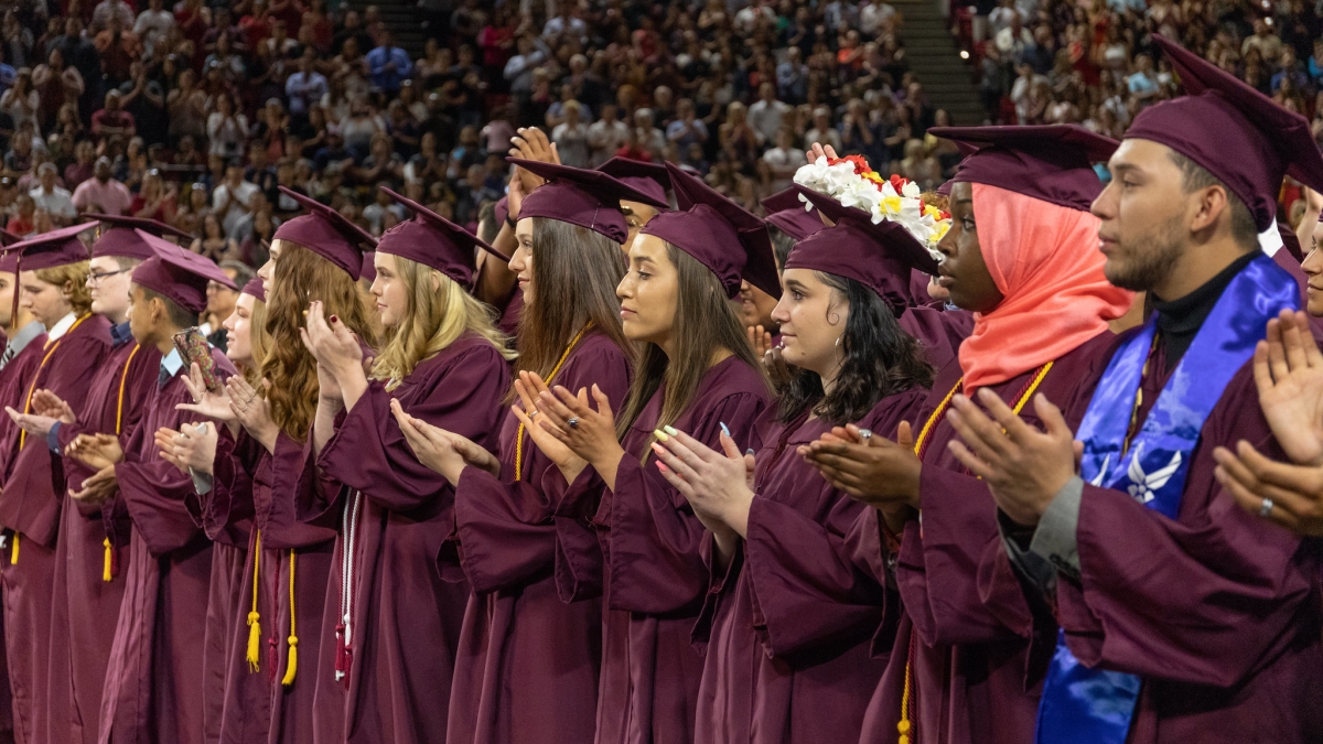 Students in maroon caps and gowns clap