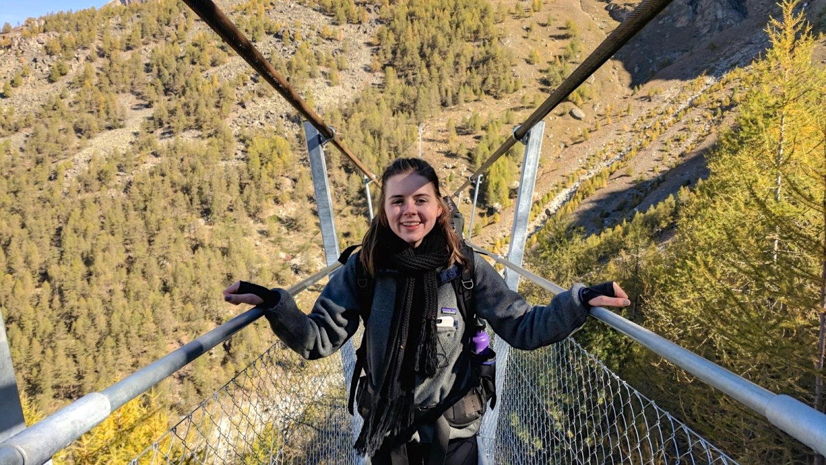 ASU alumna Azalea Thomson smiling on a narrow bridge in Switzerland, with a green, mountainous terrain in the background.