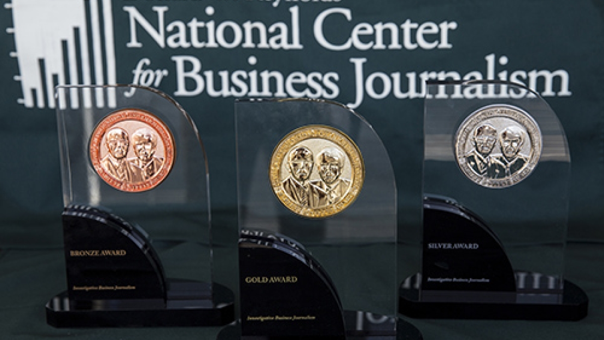 Awards made of glass and metal on a table in front of a sign that reads "Donald W. Reynolds National Cente for Business Journalism."