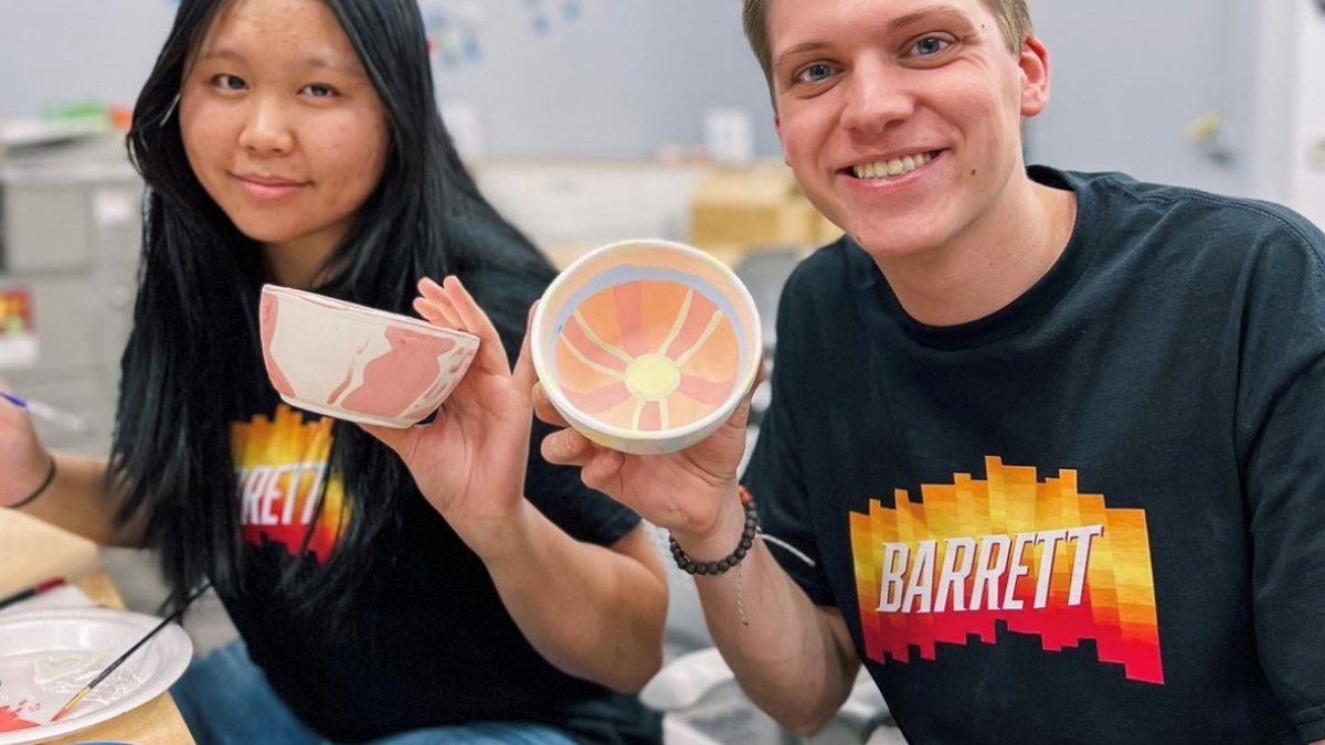Two ASU Barrett Honors College students hold up painted ceramic bowls and smile.