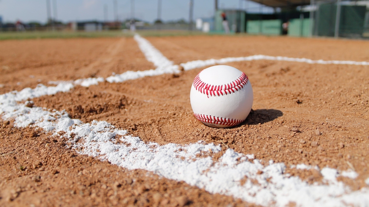 A baseball placed between white lines in the dirt on a playing field.