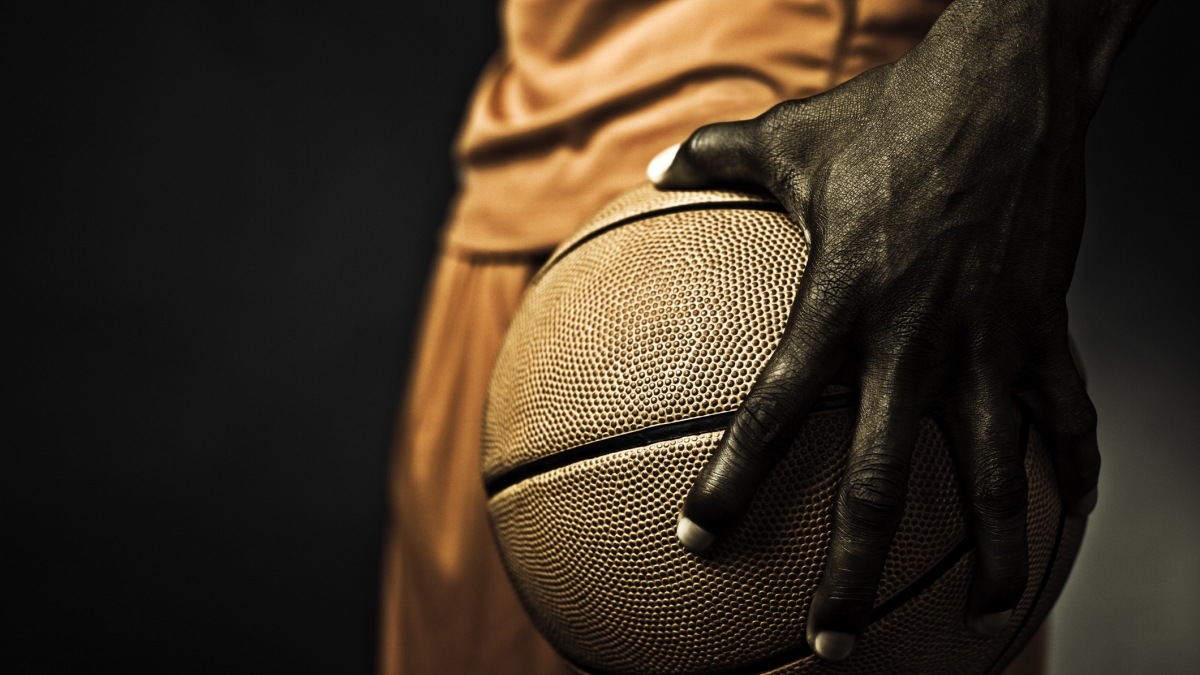 The hand of a Black basketball player gripping a basketball.