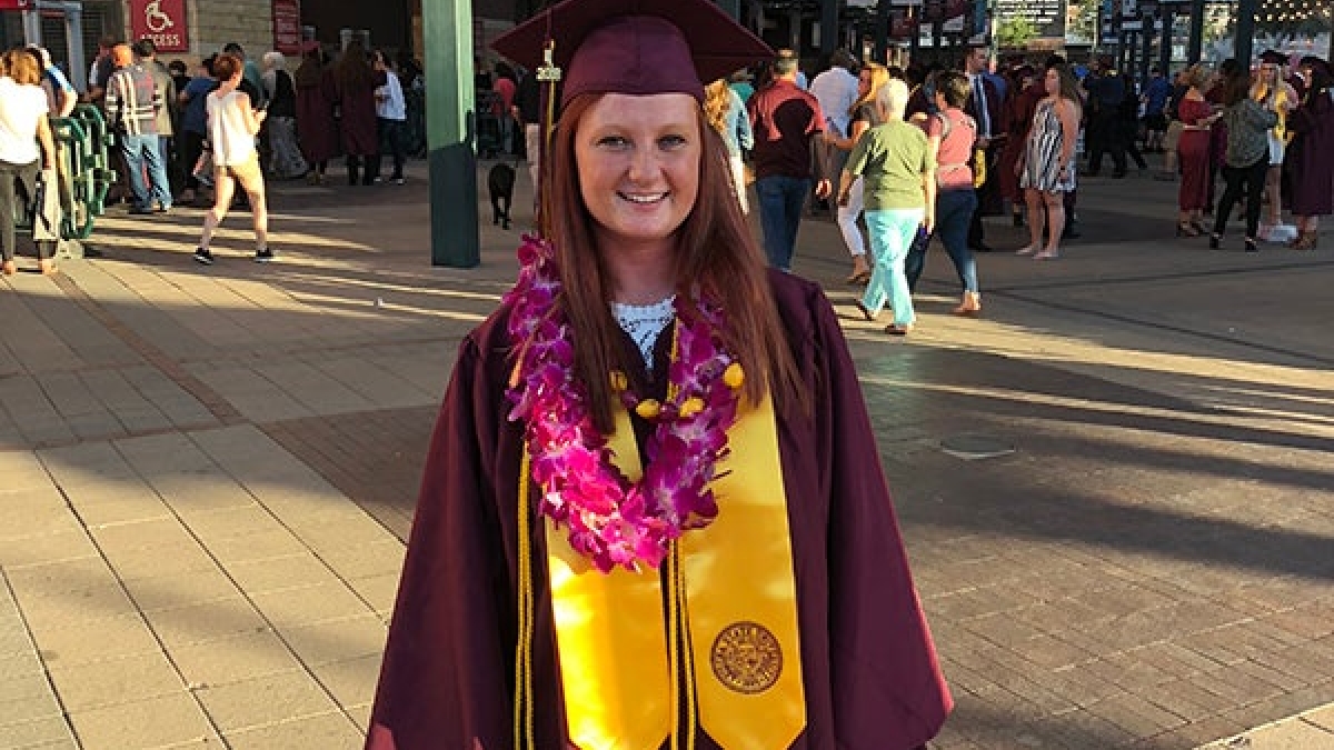 Brianna Barber poses in her graduation regalia which is a maroon robe and cap and gold with a gold sto