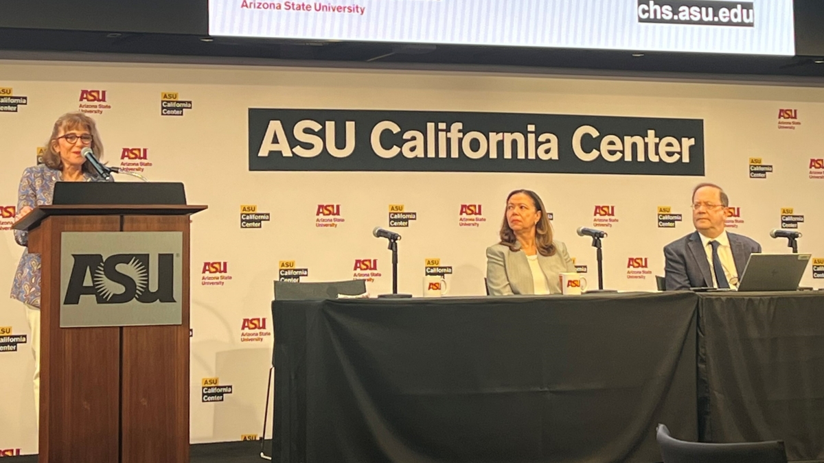 Woman speaking into microphone behind a lectern on a stage on which two other people are seated behind a table. A sign behind them reads "ASU California Center."