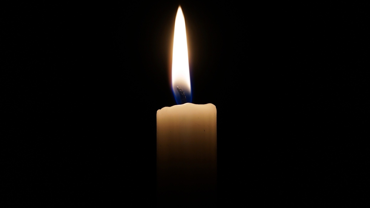 A tall flame burns atop a thin white candle against a black background.