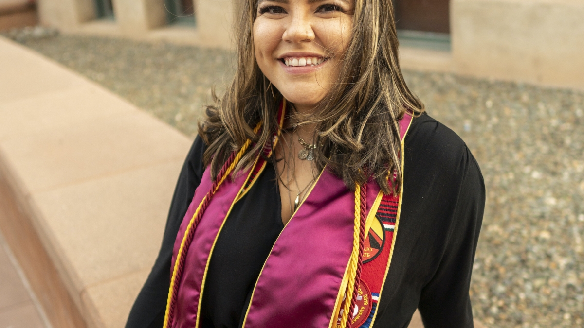 Carla Naranjo sits near Old Main wearing her graduation stoles and cords